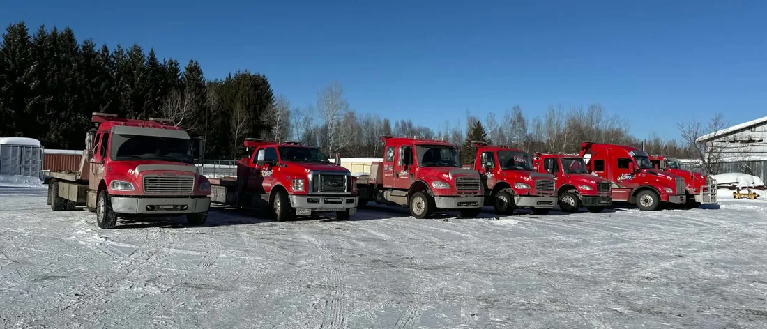 Sept camions rouges de Remorquage Gilbert alignés dans la cour enneigée de l’entreprise, à Shawinigan